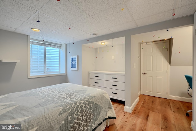 bedroom featuring light wood-style flooring, baseboards, and a drop ceiling