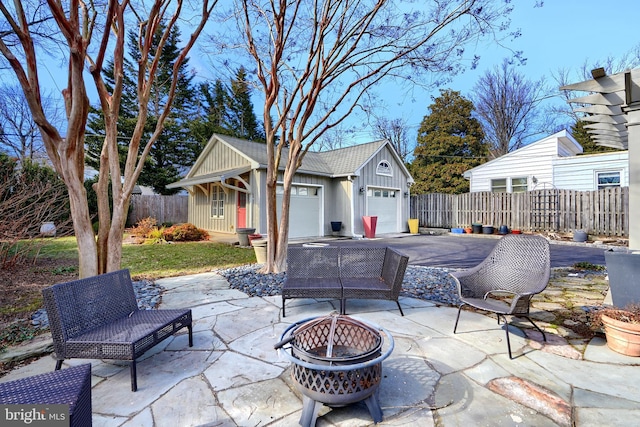 view of patio / terrace with a garage, an outdoor fire pit, fence, and driveway