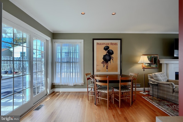 dining space with a fireplace, visible vents, baseboards, light wood-type flooring, and crown molding