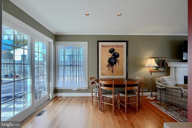 dining room featuring a fireplace, visible vents, light wood-style flooring, ornamental molding, and baseboards