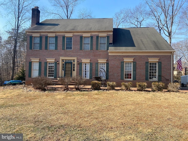 view of front of home with a front yard, a chimney, and brick siding