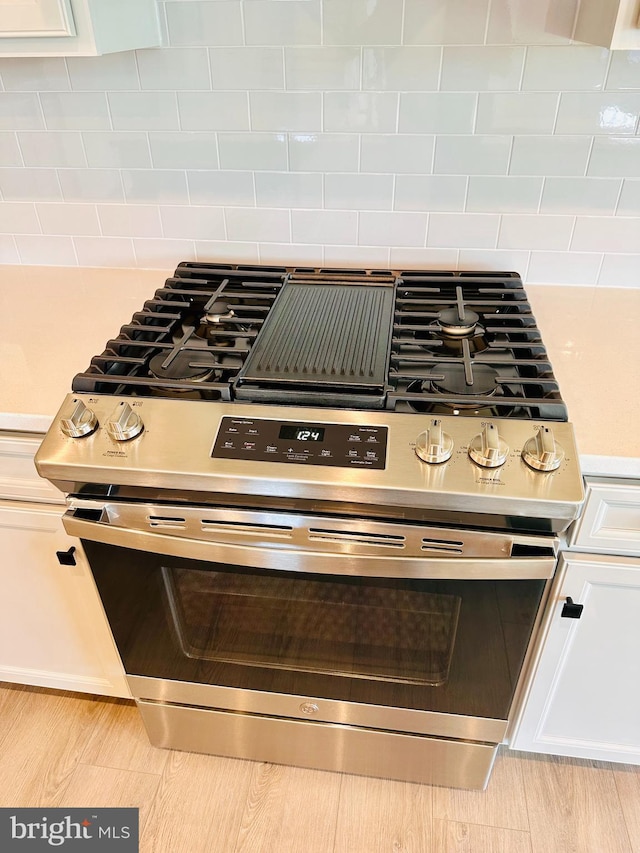 interior details featuring stainless steel range with gas cooktop, white cabinets, and decorative backsplash