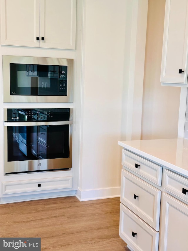 kitchen with light wood-type flooring, white cabinets, and appliances with stainless steel finishes