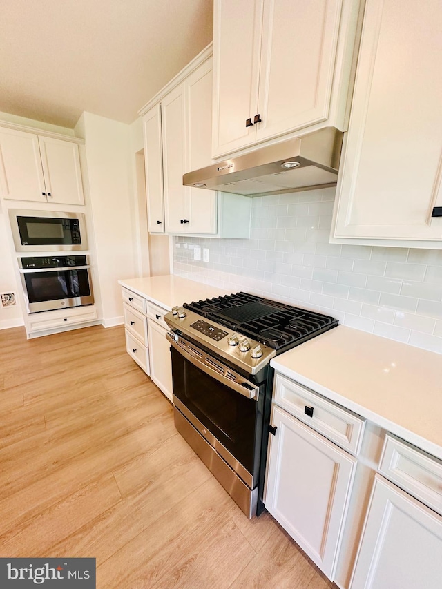 kitchen featuring stainless steel appliances, backsplash, white cabinets, and light hardwood / wood-style floors