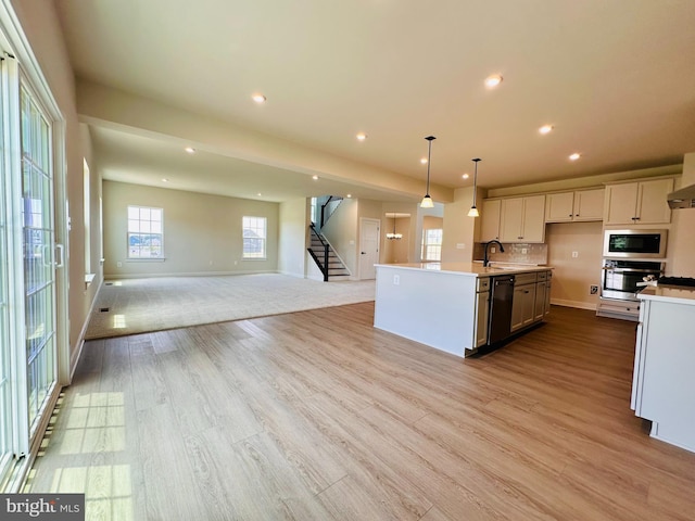 kitchen featuring built in microwave, stainless steel oven, decorative light fixtures, dishwasher, and a kitchen island with sink