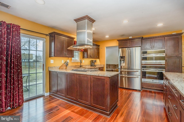 kitchen with island range hood, dark wood-type flooring, light stone countertops, and appliances with stainless steel finishes