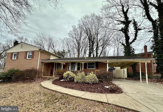 view of front facade featuring driveway, brick siding, a chimney, and an attached carport