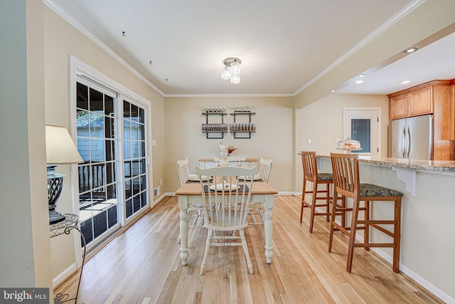 dining area with ornamental molding, light wood-style flooring, and baseboards