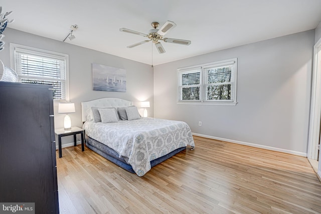 bedroom with multiple windows, light wood-type flooring, a ceiling fan, and baseboards