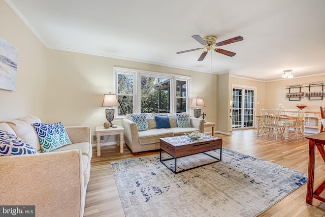 living area with crown molding, light wood-style flooring, baseboards, and ceiling fan