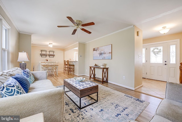 living room featuring ornamental molding, baseboards, light wood finished floors, and a ceiling fan