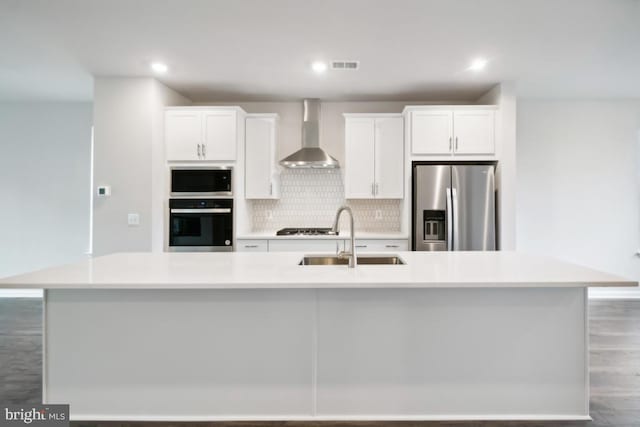 kitchen with a spacious island, wall chimney exhaust hood, sink, white cabinetry, and appliances with stainless steel finishes