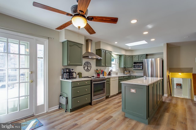 kitchen with green cabinetry, light wood-type flooring, appliances with stainless steel finishes, a kitchen island, and wall chimney range hood