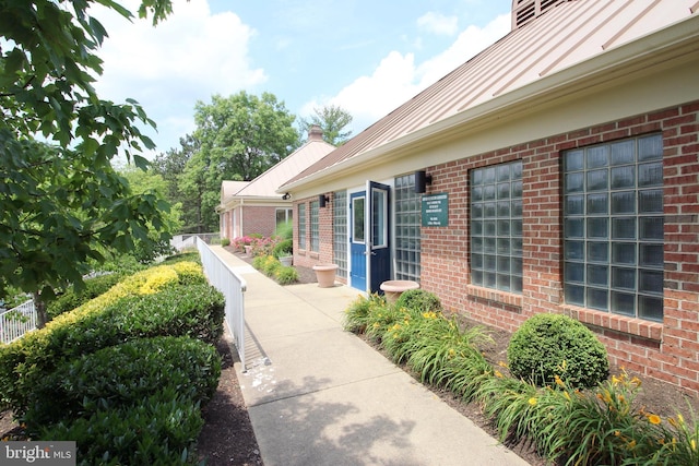 property entrance featuring a standing seam roof, fence, and brick siding