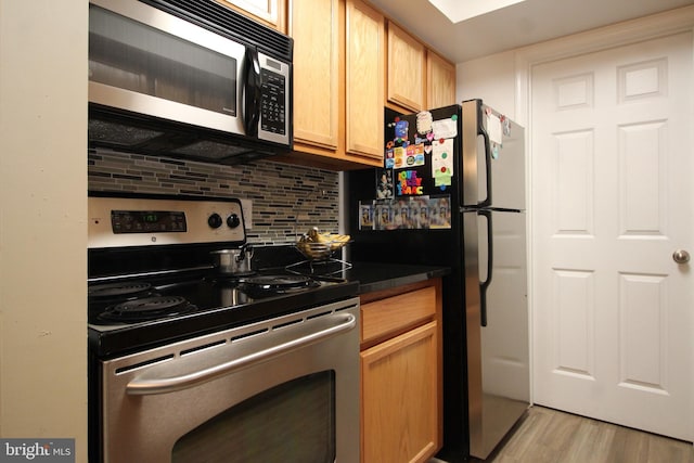 kitchen featuring light wood finished floors, decorative backsplash, dark countertops, appliances with stainless steel finishes, and light brown cabinetry