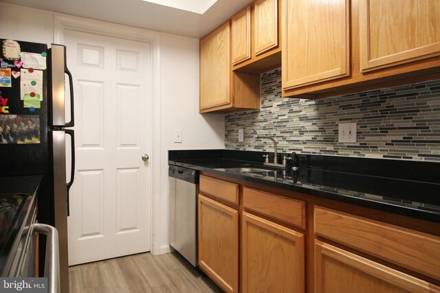 kitchen featuring light wood-style floors, tasteful backsplash, appliances with stainless steel finishes, and a sink