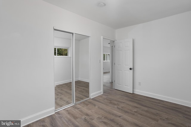 unfurnished bedroom featuring a closet, multiple windows, baseboards, and wood finished floors