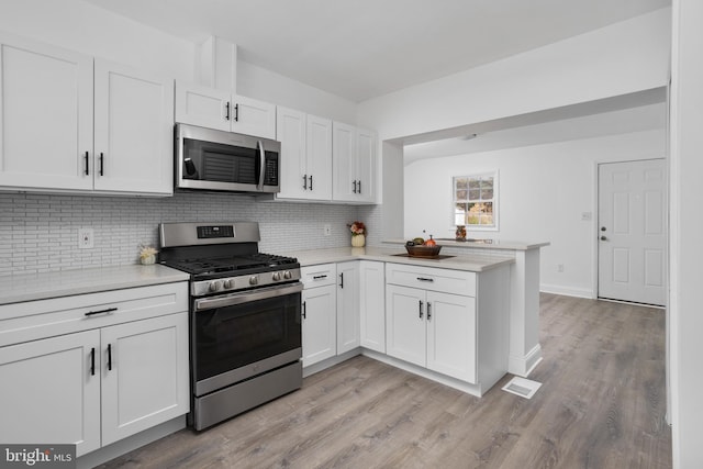 kitchen featuring appliances with stainless steel finishes, light countertops, a peninsula, and white cabinetry