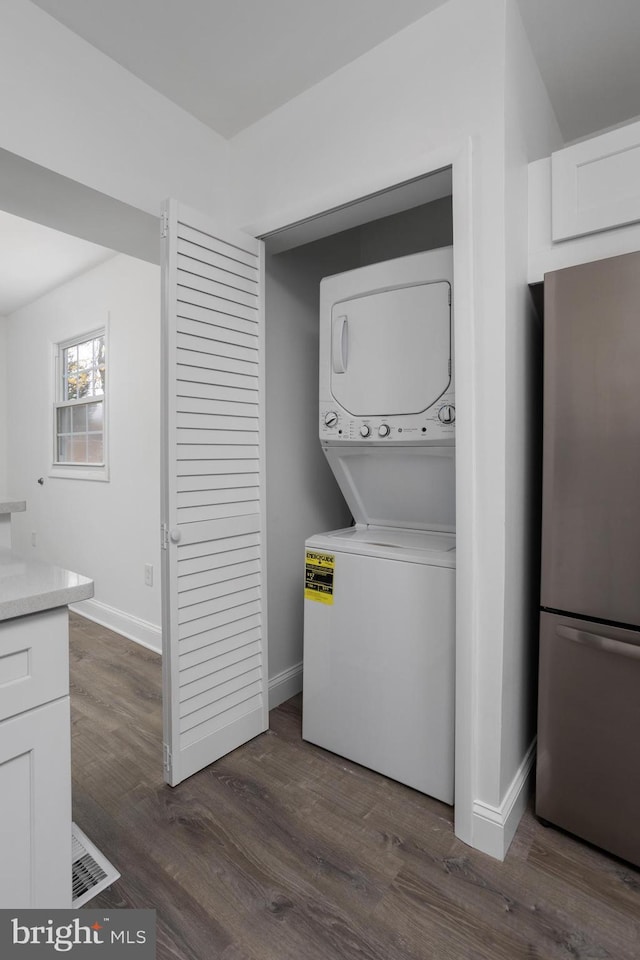 laundry room with dark wood-style floors, stacked washer and clothes dryer, baseboards, and laundry area