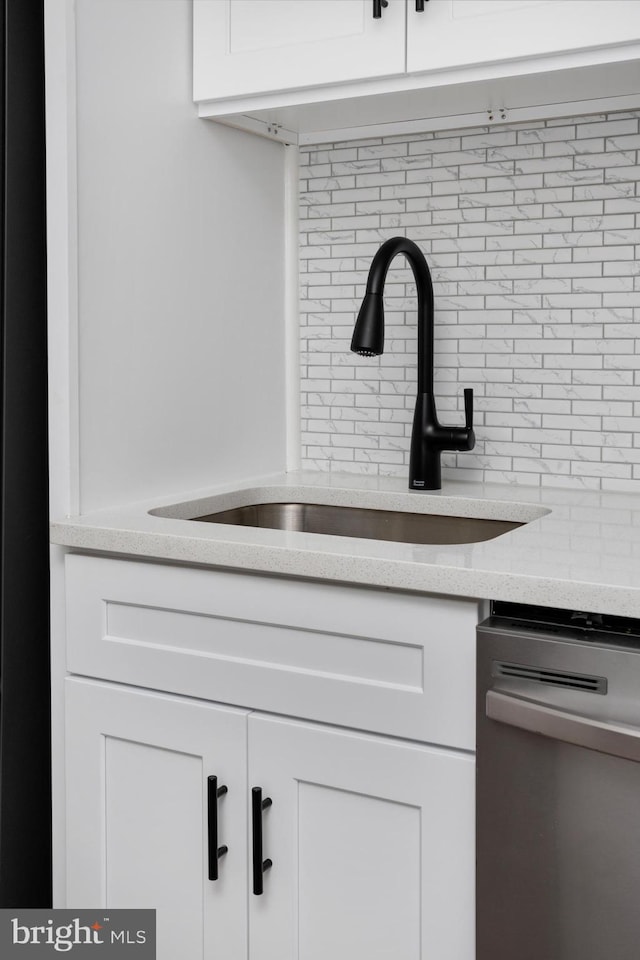 interior details featuring stainless steel dishwasher, a sink, white cabinets, and decorative backsplash