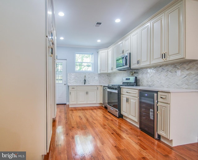 kitchen with sink, light hardwood / wood-style flooring, appliances with stainless steel finishes, backsplash, and beverage cooler