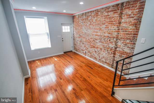 entryway featuring hardwood / wood-style floors, ornamental molding, and brick wall