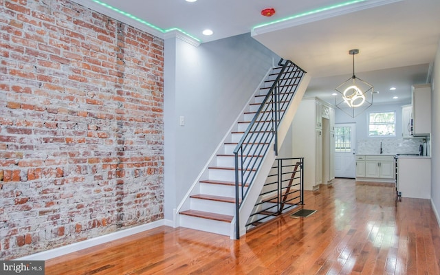 staircase featuring ornamental molding, wood-type flooring, and brick wall