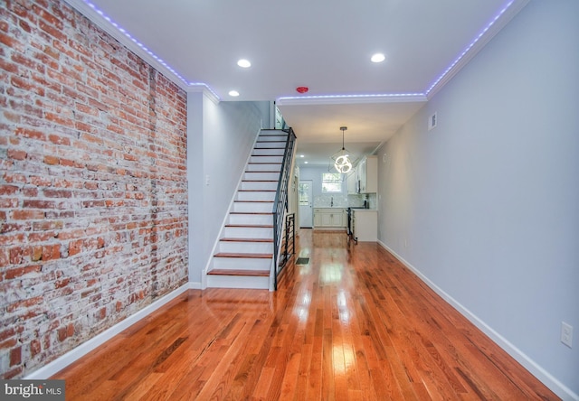 corridor with ornamental molding, light hardwood / wood-style floors, and brick wall