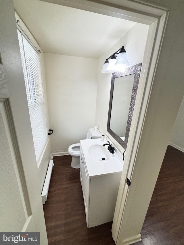 bathroom featuring baseboards, toilet, wood finished floors, vanity, and a baseboard heating unit