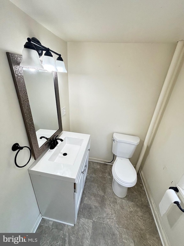 half bath with baseboards, vanity, and toilet