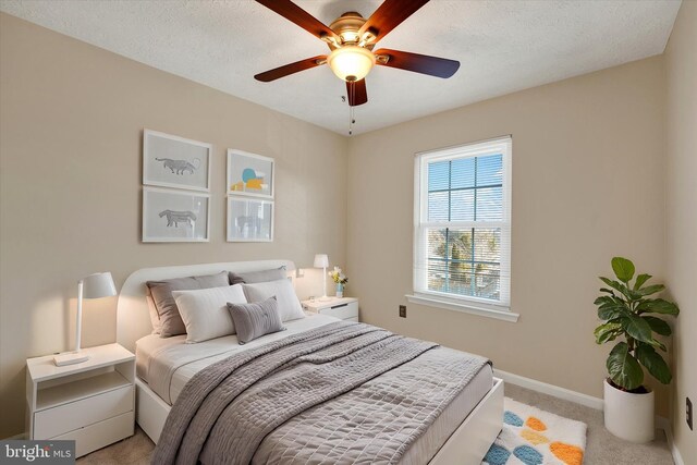 bedroom featuring light carpet, ceiling fan, baseboards, and a textured ceiling