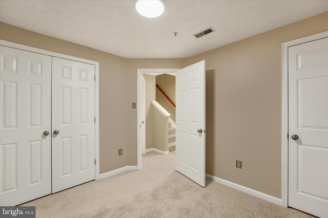 unfurnished bedroom with baseboards, visible vents, light colored carpet, a textured ceiling, and a closet