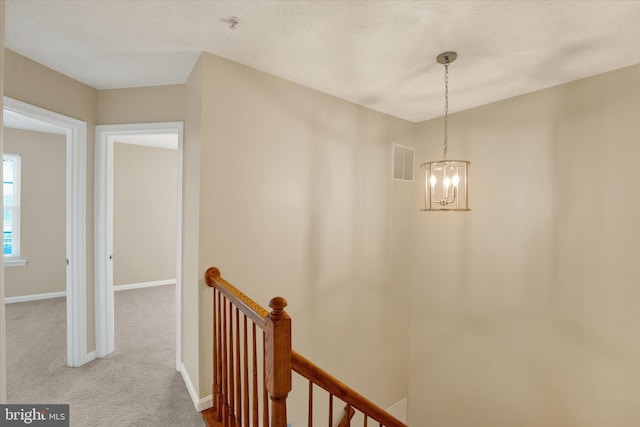 corridor with baseboards, visible vents, carpet flooring, an upstairs landing, and a chandelier