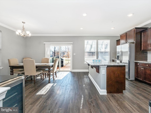 kitchen featuring light stone counters, dark brown cabinetry, decorative light fixtures, a center island, and stainless steel fridge