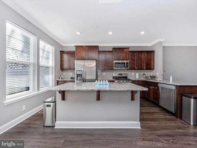 kitchen with appliances with stainless steel finishes, a breakfast bar, a kitchen island, and dark hardwood / wood-style flooring