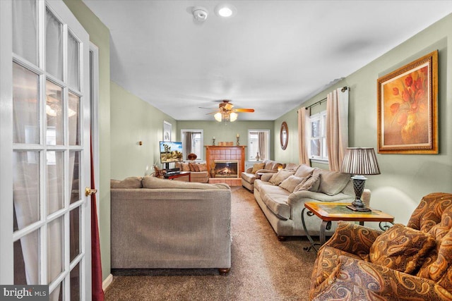 living room featuring ceiling fan, carpet flooring, a tiled fireplace, and a healthy amount of sunlight