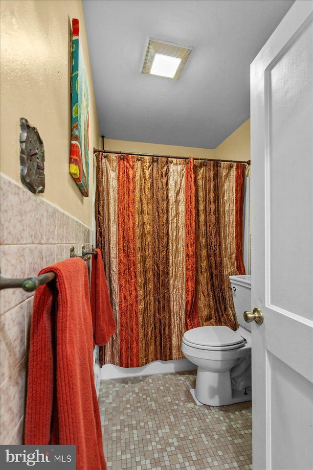 bathroom featuring tile patterned floors, toilet, and tile walls