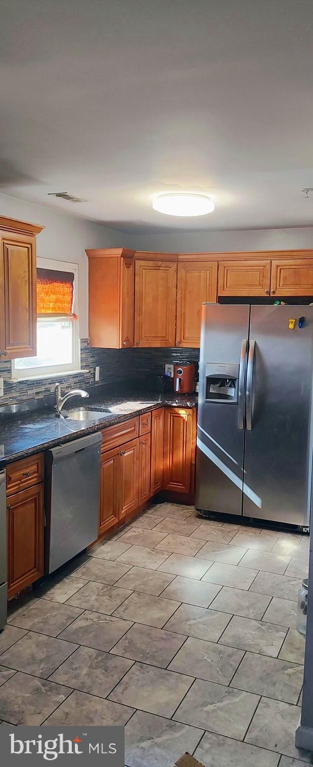 kitchen with stainless steel appliances, a sink, visible vents, tasteful backsplash, and brown cabinetry