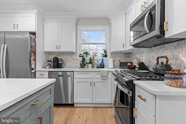 kitchen with backsplash, white cabinets, stainless steel appliances, light stone countertops, and light wood-type flooring