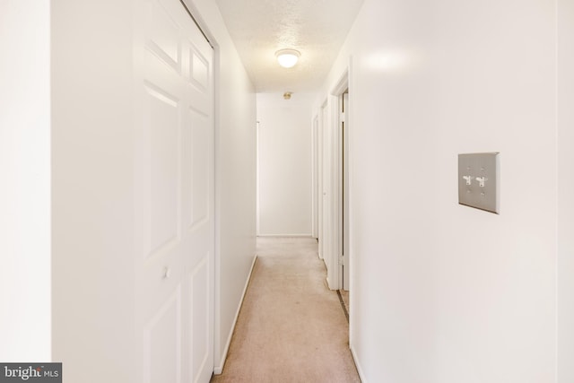 hall featuring light carpet, baseboards, and a textured ceiling