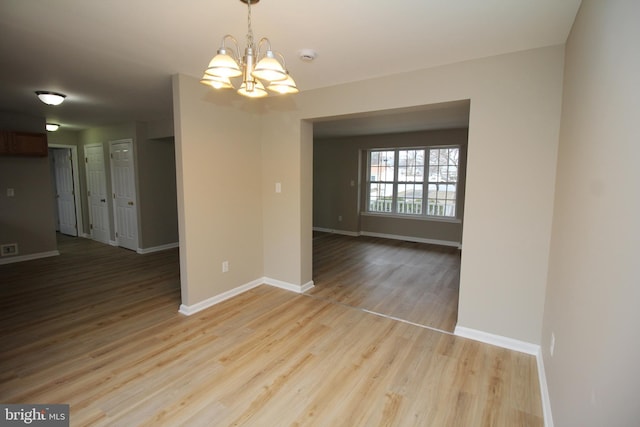 spare room featuring a chandelier and light wood-type flooring