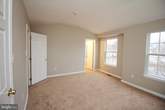 unfurnished bedroom with multiple windows, vaulted ceiling, light carpet, and ensuite bath