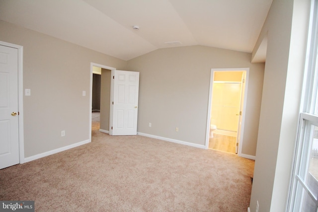 unfurnished bedroom with lofted ceiling, connected bathroom, and light colored carpet