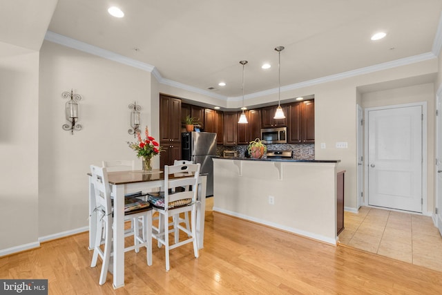 kitchen featuring appliances with stainless steel finishes, tasteful backsplash, a breakfast bar area, decorative light fixtures, and light hardwood / wood-style floors