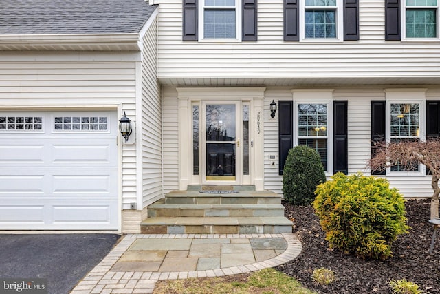 view of exterior entry featuring a garage and a shingled roof