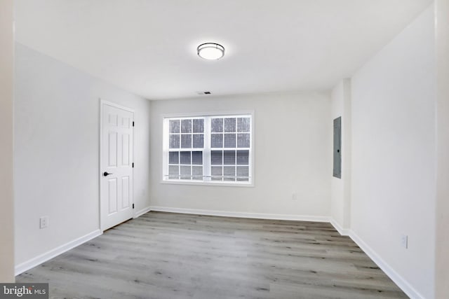 empty room featuring electric panel, visible vents, baseboards, and wood finished floors