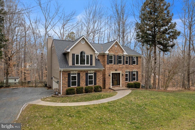 view of front of house featuring a chimney, aphalt driveway, fence, a front lawn, and brick siding