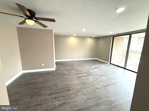 unfurnished room featuring dark wood-type flooring, a wall of windows, and ceiling fan