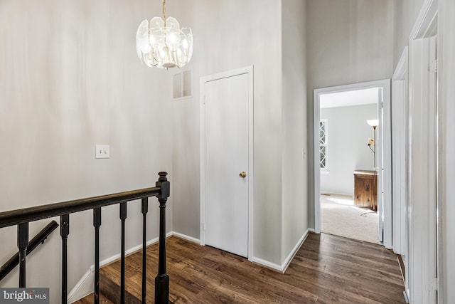 hallway with visible vents, an upstairs landing, baseboards, and wood finished floors