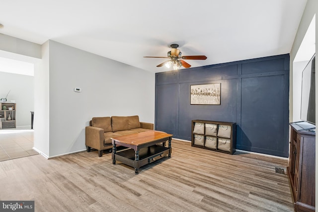 living room featuring visible vents, baseboards, ceiling fan, and light wood finished floors